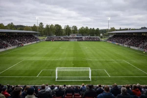 Kleines Fußballstadion in Skandinavien mit grünem Rasen und Zuschauern bei Tageslicht