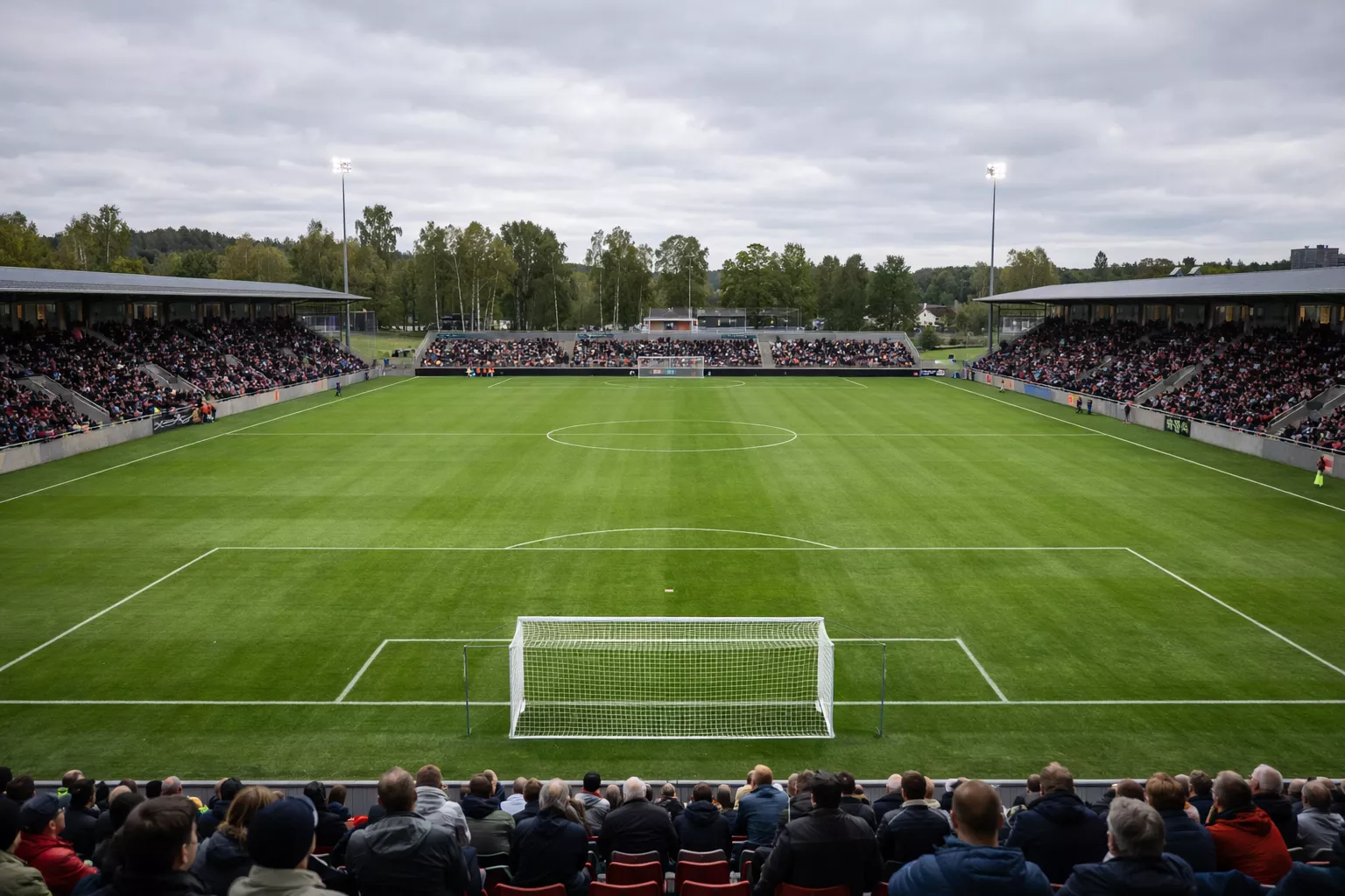 Kleines Fußballstadion in Skandinavien mit grünem Rasen und Zuschauern bei Tageslicht