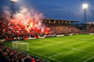 Fußballspiel in einem mittelgroßen Stadion mit stimmungsvoller Fankurve bei Flutlicht